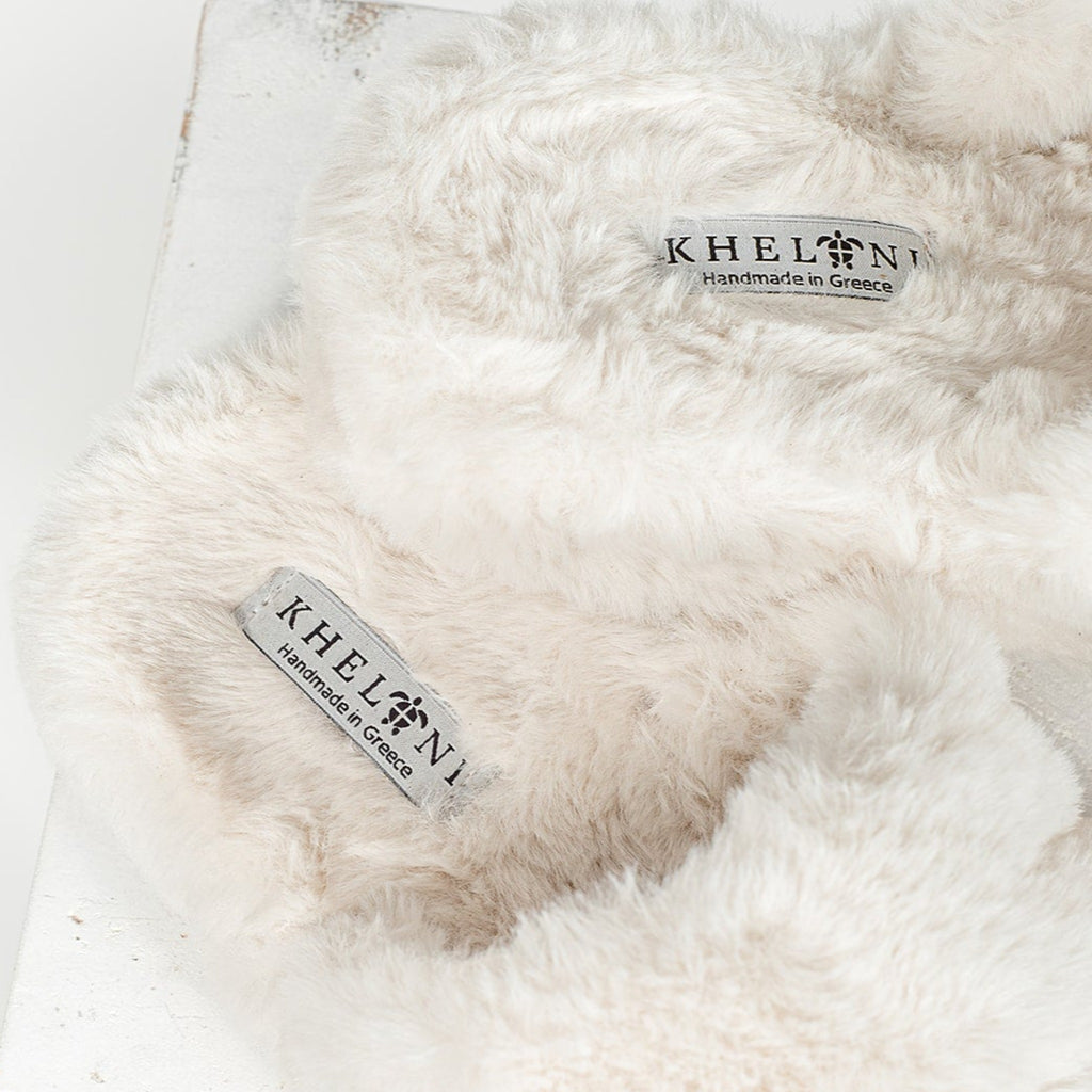 Close up of Kheloni logo on footbed of cream colored soft faux slippers in a contemporary setting.