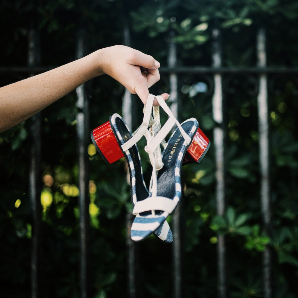Woman holding handmade Greek sandal with blue and white linen and a fire red heel.